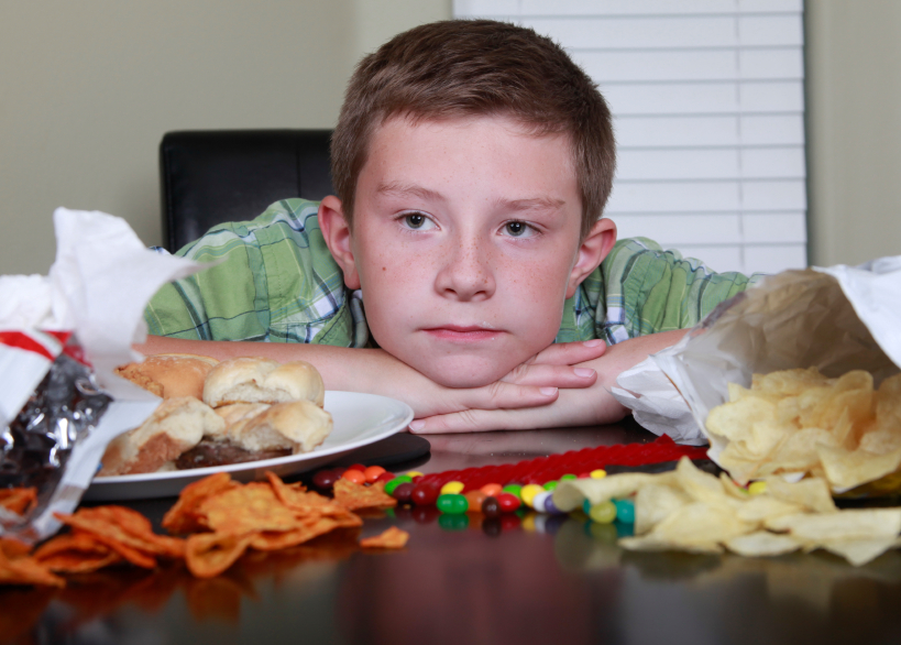 A boy putting his head on the table with food in front of him.