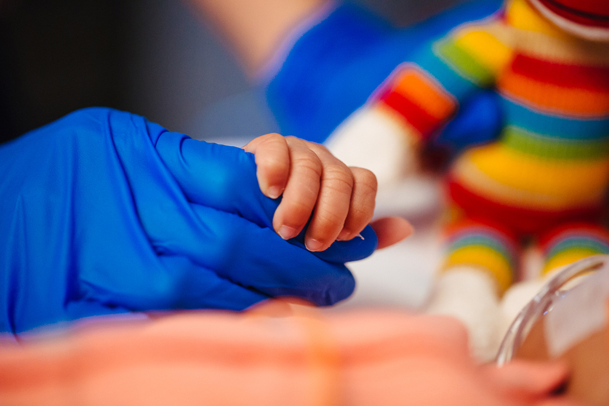 Adult Hand in Glove holding a Baby's Hand.