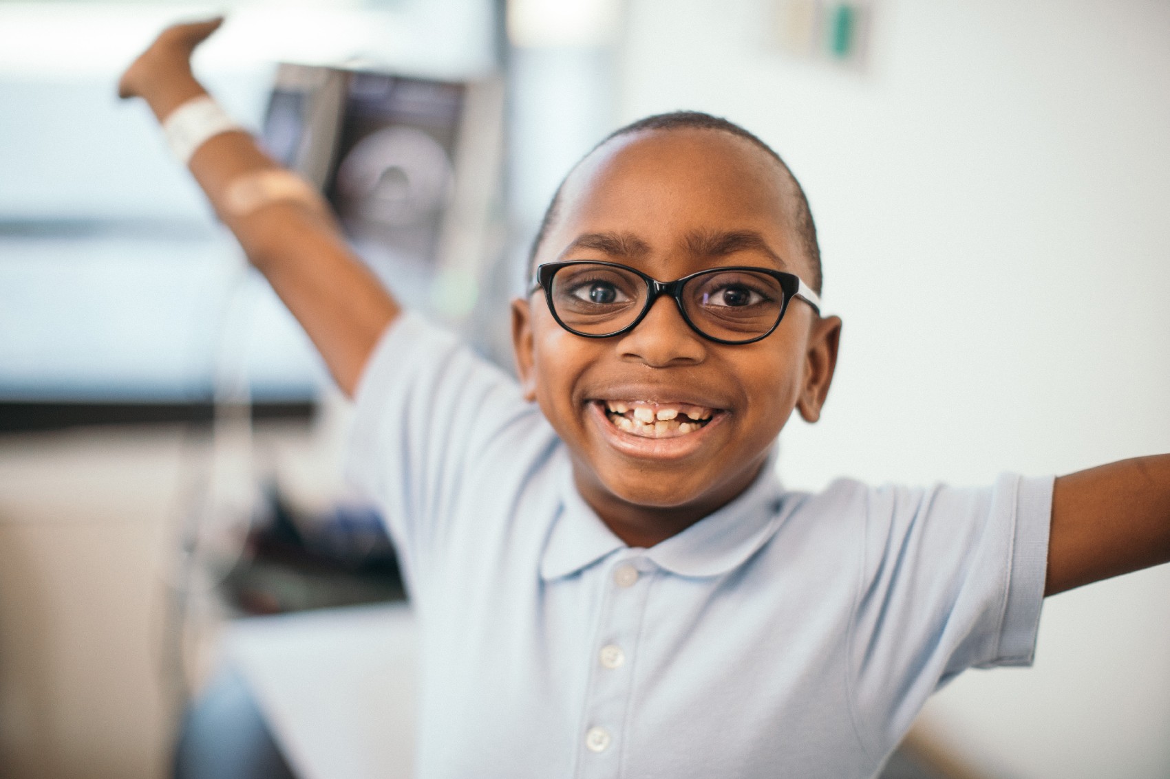 Happy Boy with arms raised waiting in a exam room.
