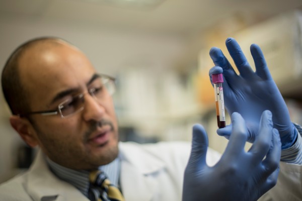 Male provider wearing blue gloves holding up a vial