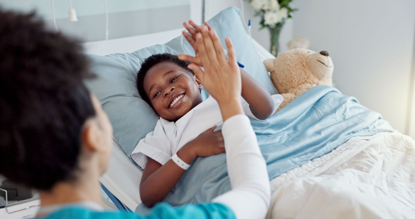 young boy in hospital bed high-fiving a provider