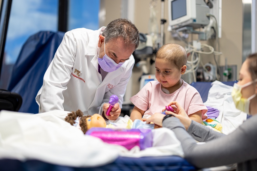 David Jacobsohn, MD, ScM, MBA, division chief of Blood and Marrow Transplantation, helps a young girl perform a medical check-up on a doll as a way to cope with her treatment.