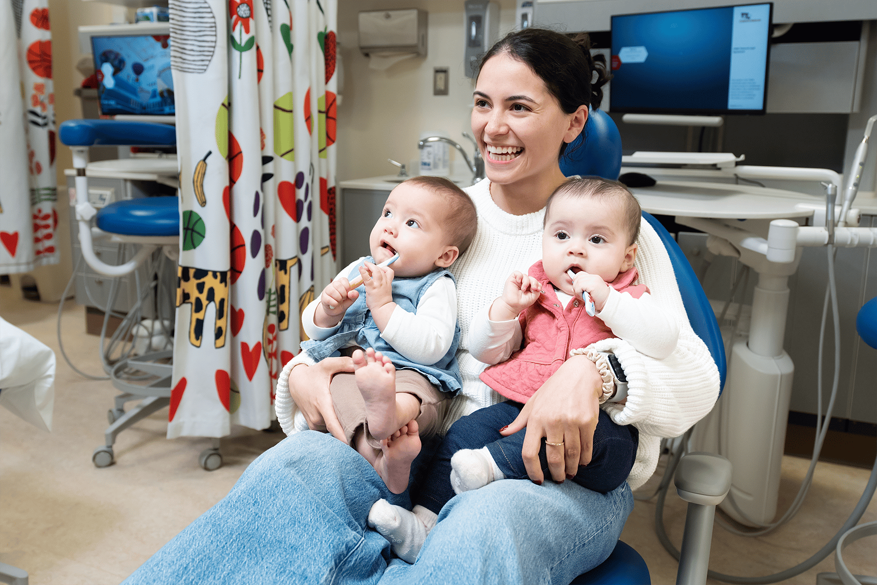 Mother with two small babies sitting in the dentist chair smiling