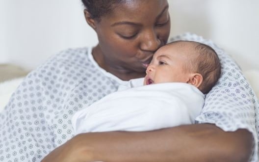 A new mom cradles her baby and kisses their head.