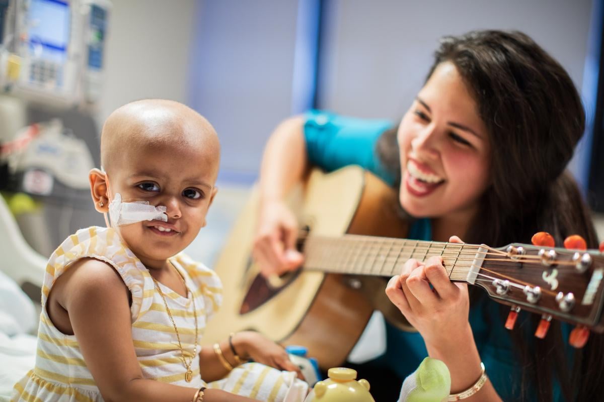 a music therapist sings and plays guitar to a patient