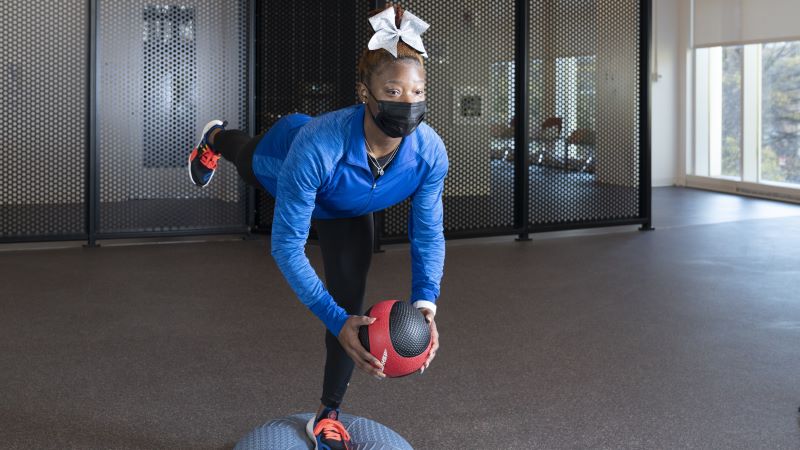 Young woman balances while holding weighted ball.