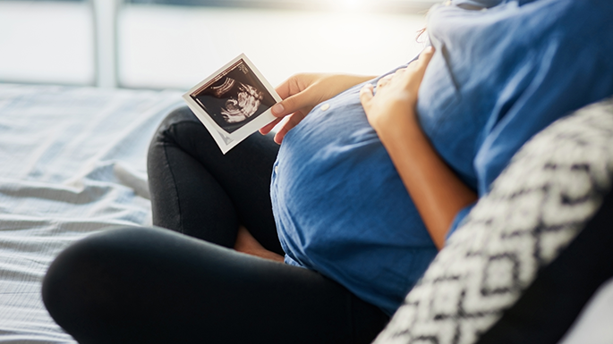pregnant woman sitting on couch holding sonogram