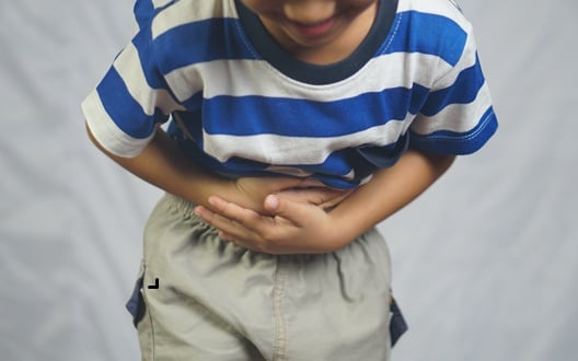 A young boy winces in pain as he bends forward holding his stomach