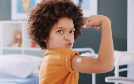 Child flexing their right arm to show off the band-aid on their bicep from getting a vaccine