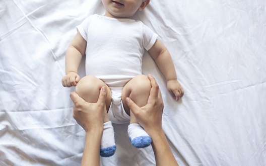 A healthcare provider holds a baby's knees and legs up to his stomach to help relieve constipation. 