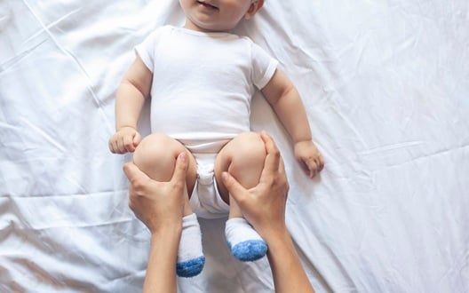 A healthcare provider holds a baby's knees and legs up to his stomach to help relieve constipation.