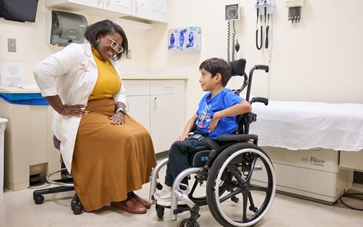 A pediatrician visits with a young boy in a wheelchair during his appointment