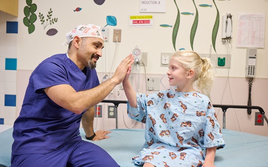A surgeon high-fives a young girl as she prepares for surgery