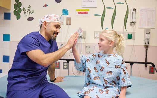 A surgeon high-fives a young girl as she prepares for surgery