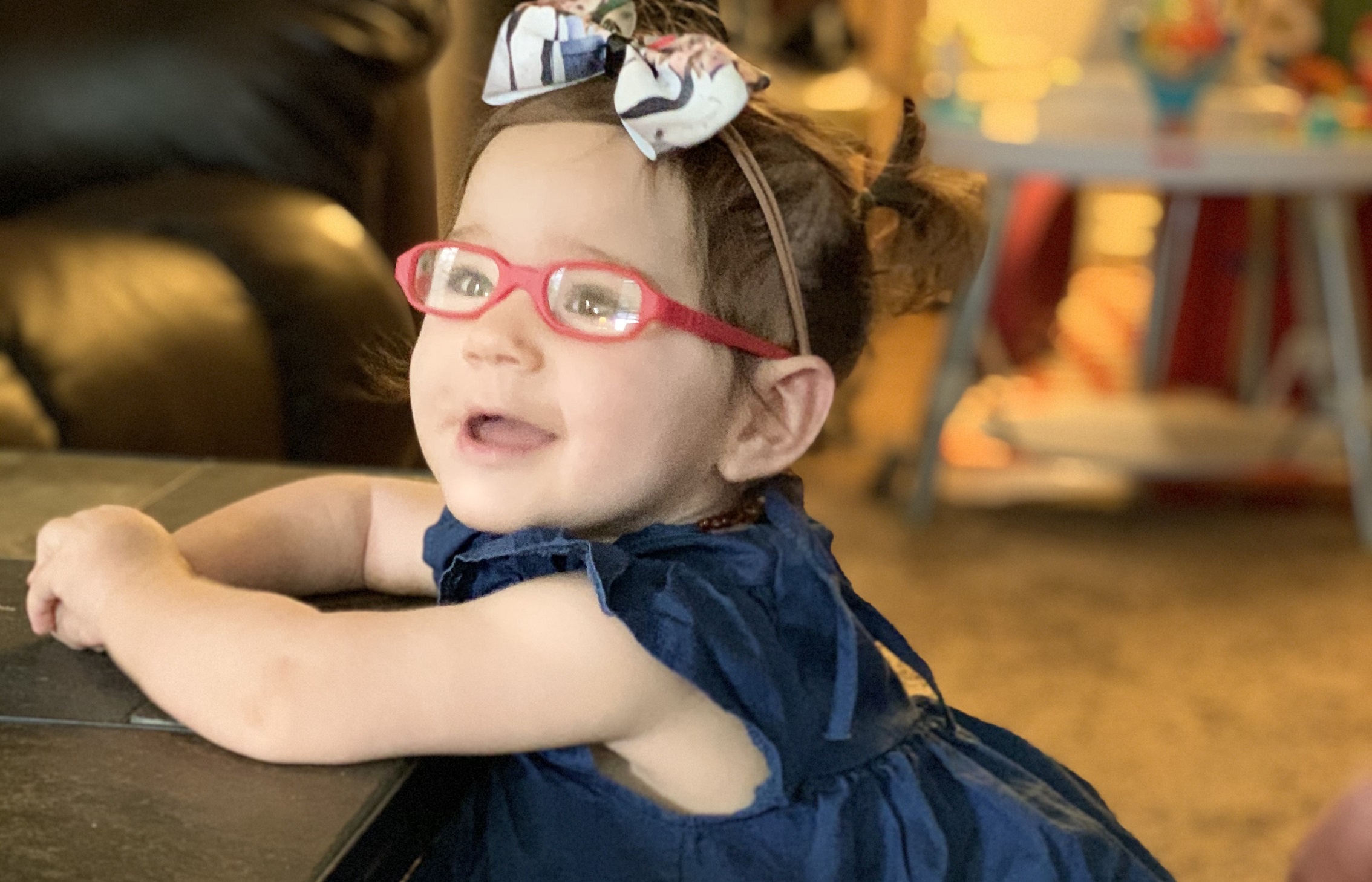 little girl wearing pink eyeglasses and hair bow smiles at camera