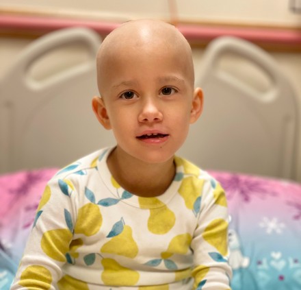 Isabel with a bald head sitting on a bed and smiling