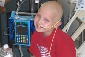 A bald young boy smiling with a tube in his nose