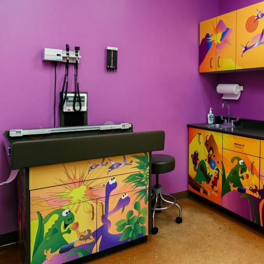 Photograph of a pediatric exam room at CNPA Bowie. The walls are purple and the cabinets are painted with dinosaurs.
