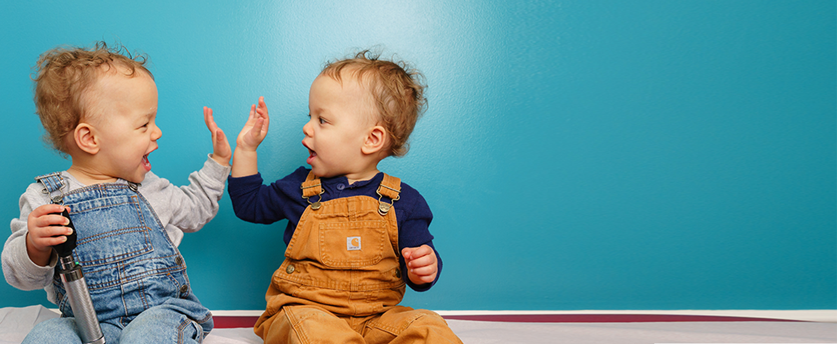 two toddlers high-fiving on exam table
