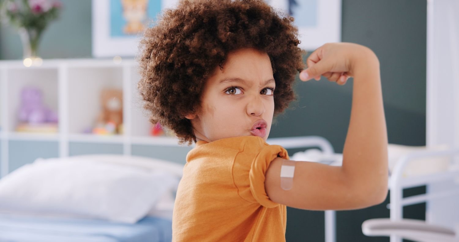 boy flexing his arm with a bandaid after receiving a vaccine