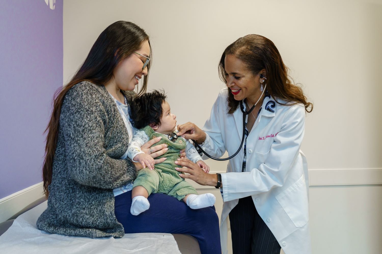 doctor examines baby sitting on mom's lap