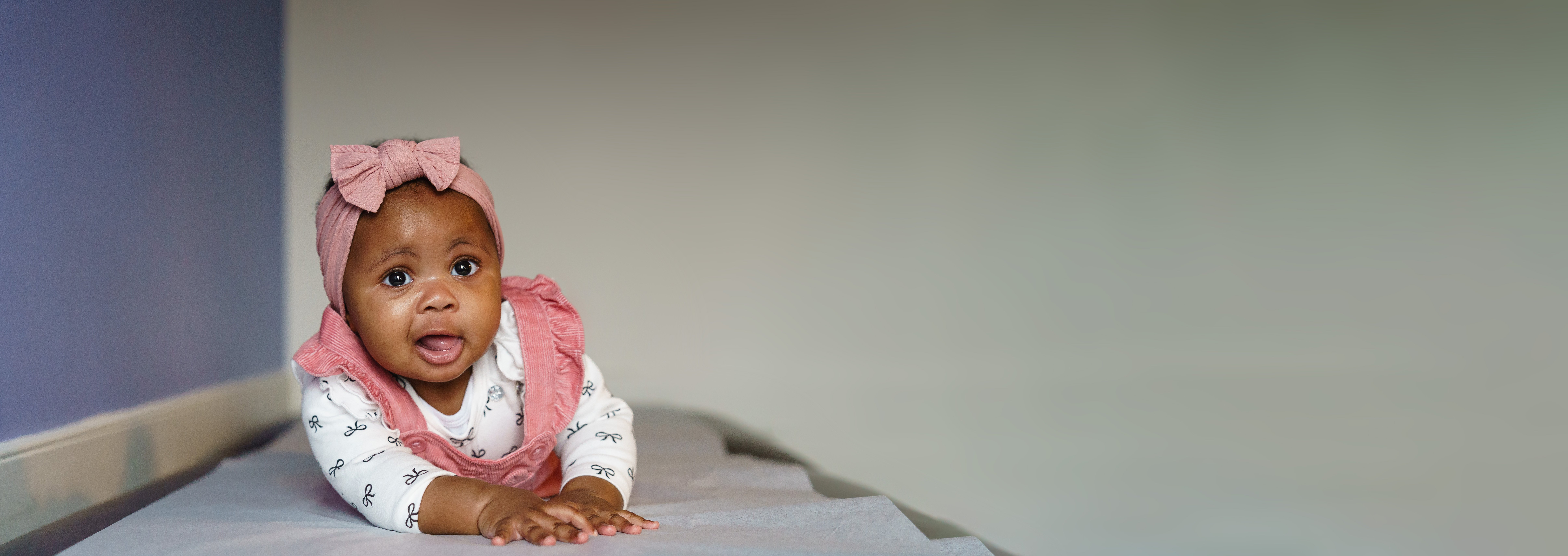 baby with pink headband on exam table