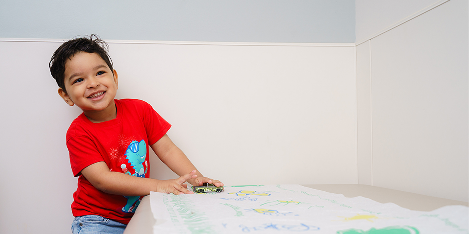 smiling boy playing with a racecar on exam table