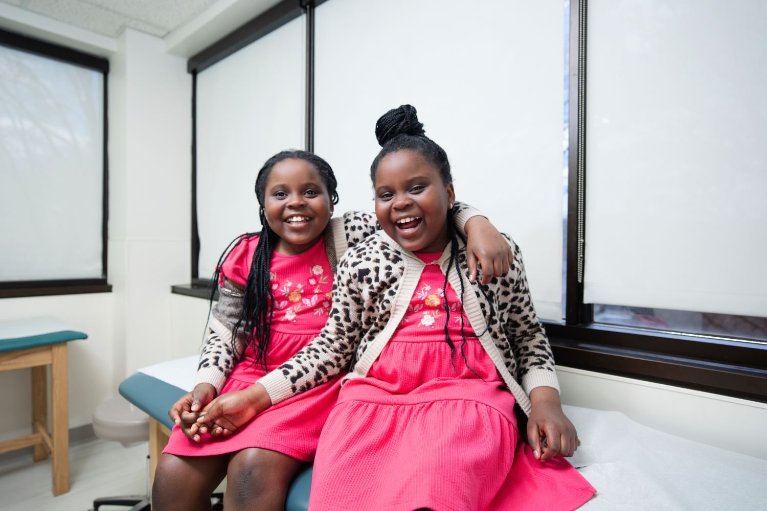 two patients in pink dresses sit on an exam table