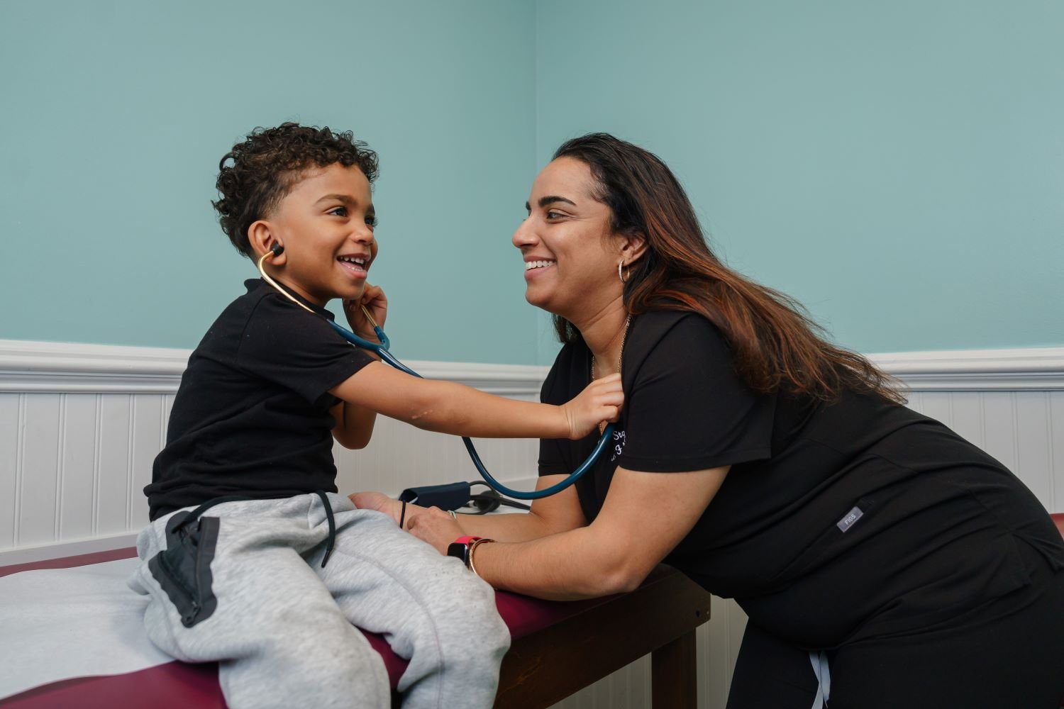 provider smiles as young patient listens to her heart with stethoscope