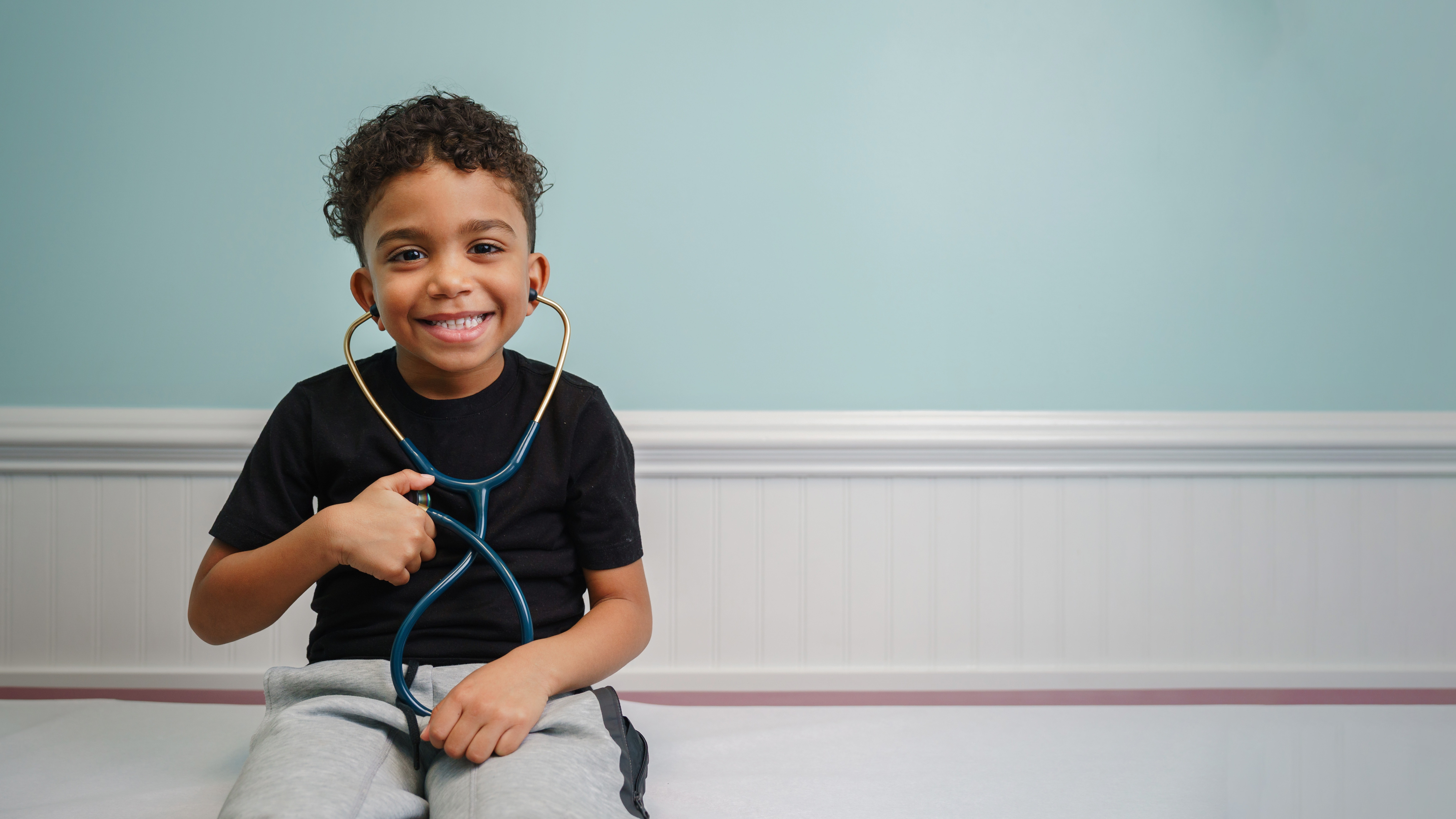 smiling boy wearing stethoscope on exam table
