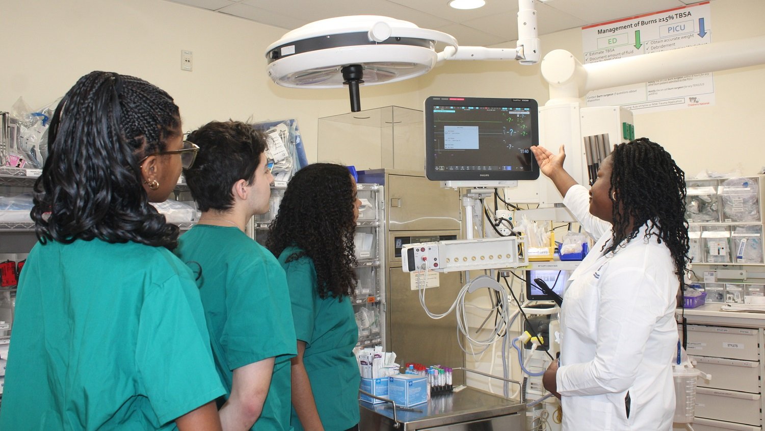 Jessica Williams, MD, explains the vital signs displayed on the monitor to the ED Research interns, demonstrating how the clinical team closely monitors a trauma patient's condition in the code room.