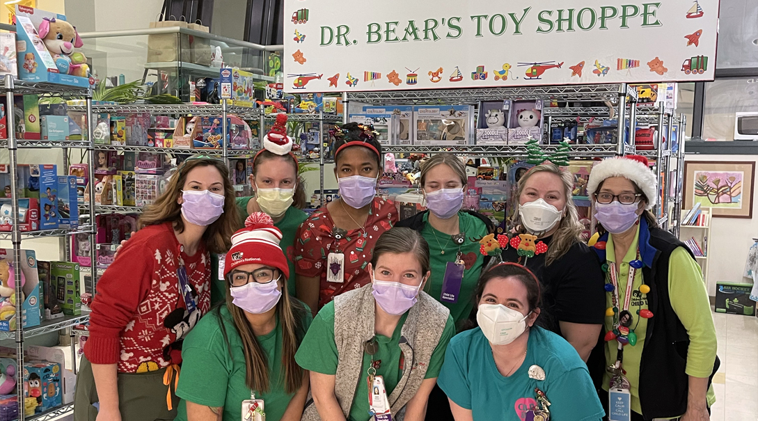 Several Hospital staff members posing next to shelves of toys in Dr. Bear's Toy Shoppe