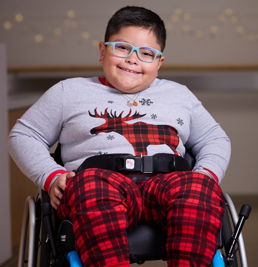 Daniel, an adolescent patient in a wheelchair, smiles at the camera while wearing holiday-themed flannels.