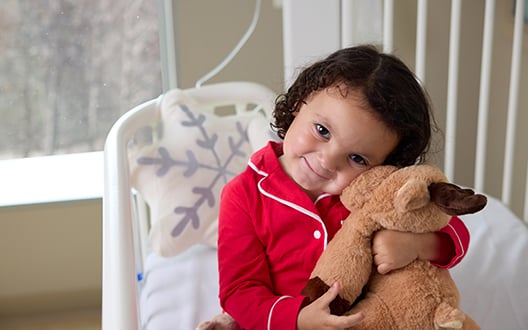 CNH patient, Emmylou, cuddles with a stuffed reindeer toy while wearing red pajamas.