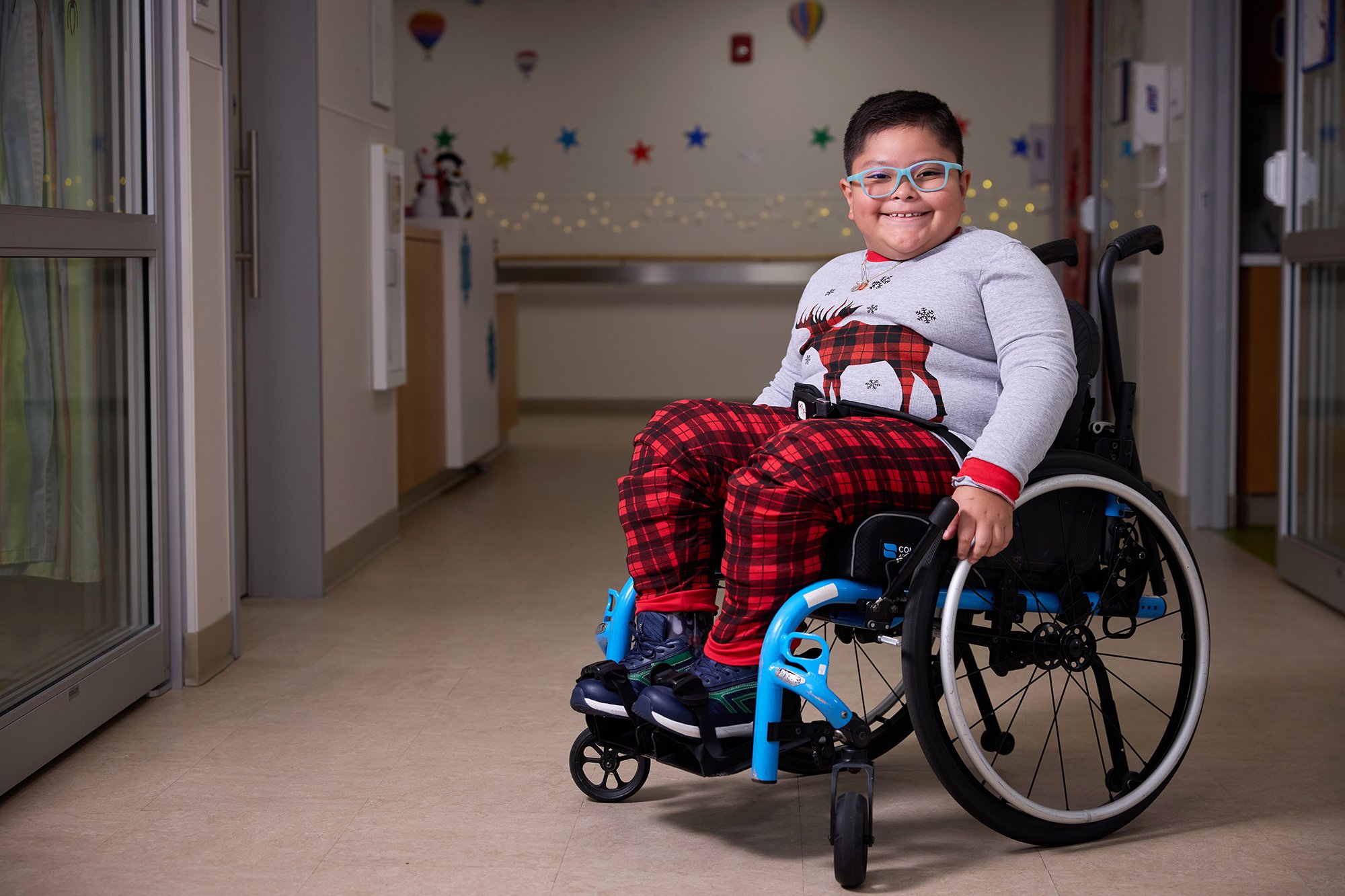 CNH patient Daniel, age 8, smiles at the camera while seated in a wheelchair and wearing winter-themed flannels.
