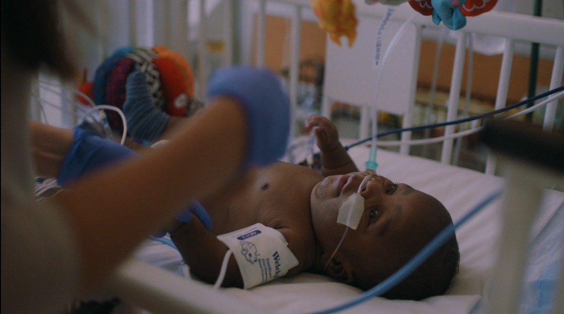 Infant lying on back in crib receiving NICU care