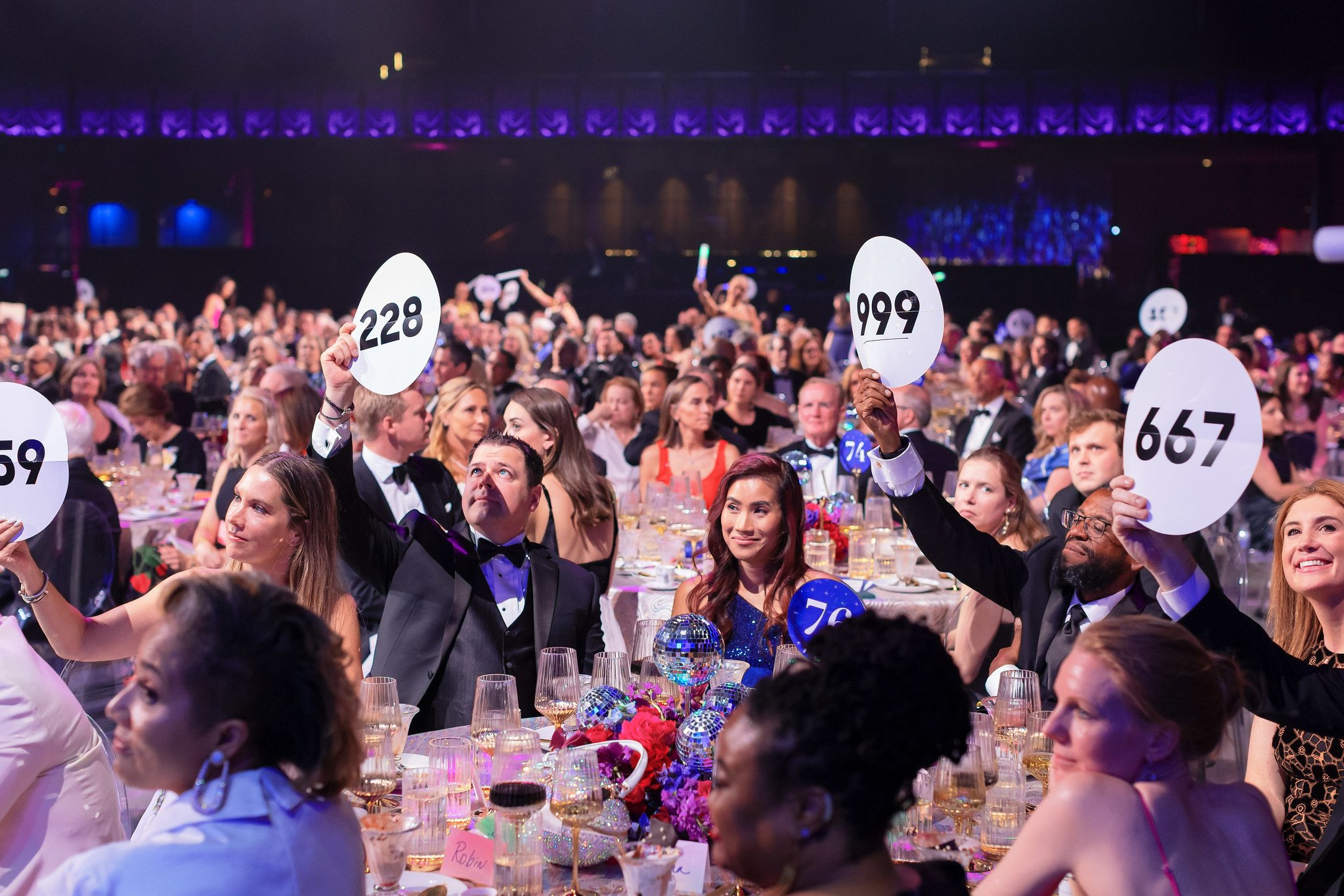 Children's Ball attendees raising auction paddles while seated at dining tables