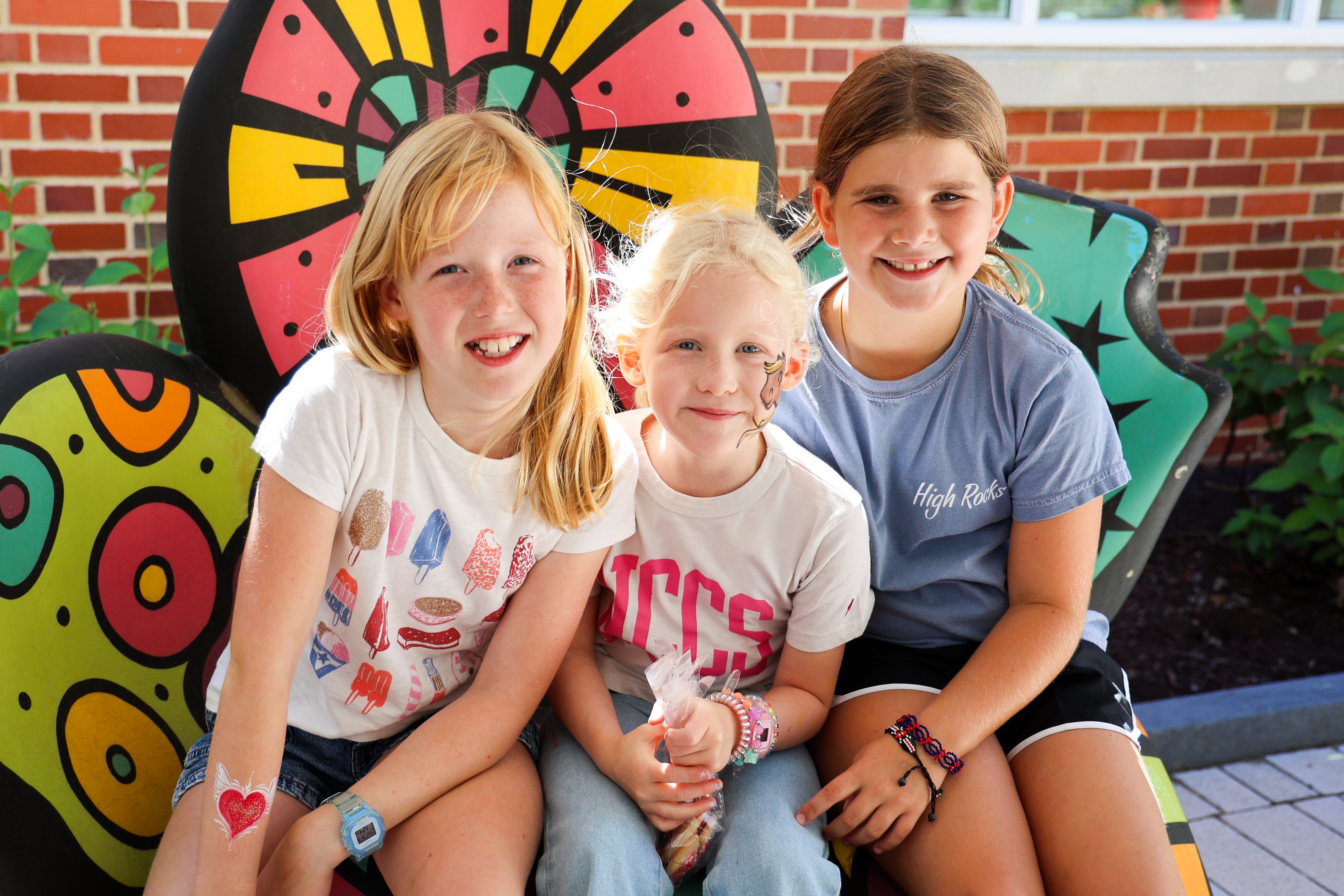 Three young children with their faces painted smile at the camera.