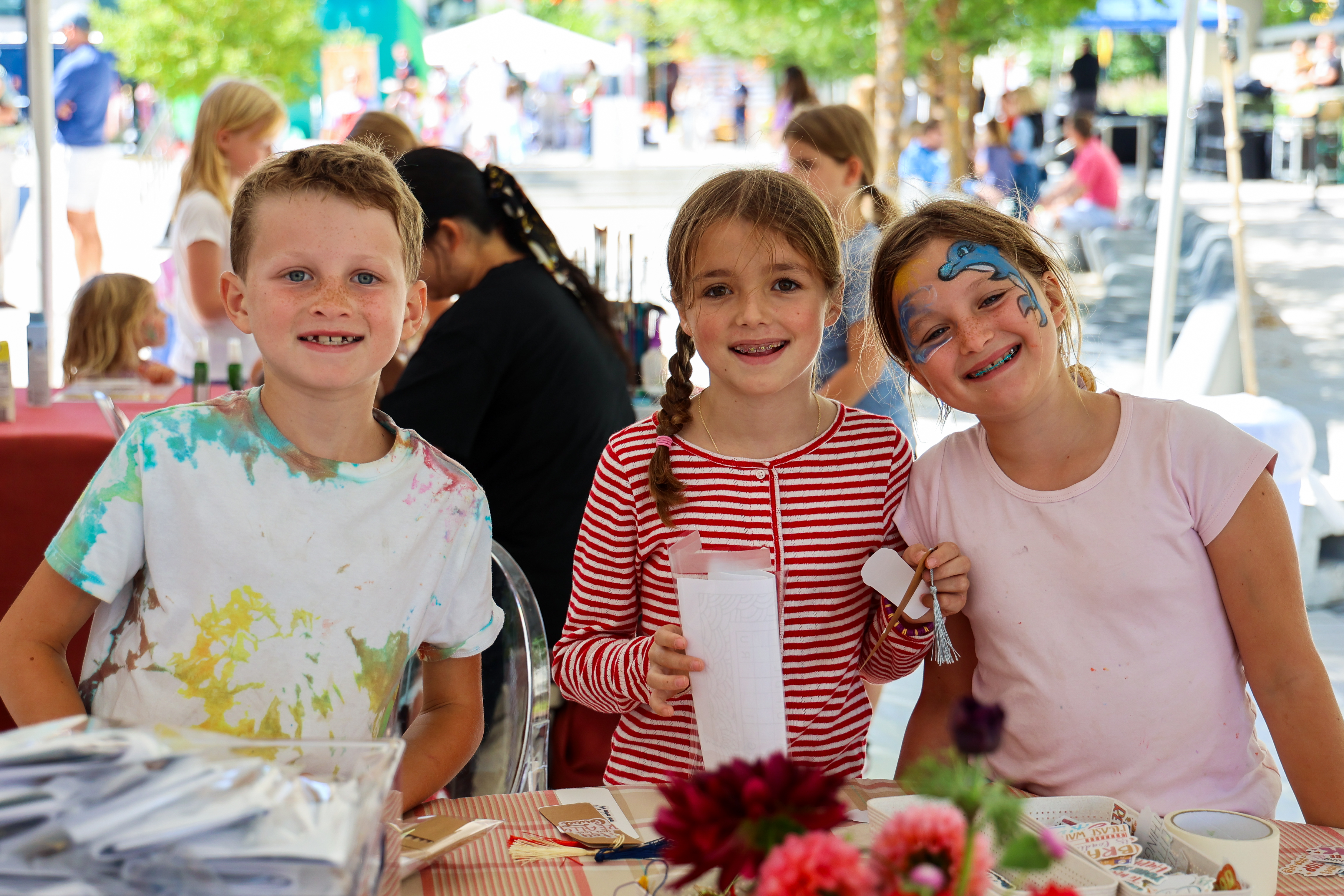 Three young children with their faces painted smile at the camera.