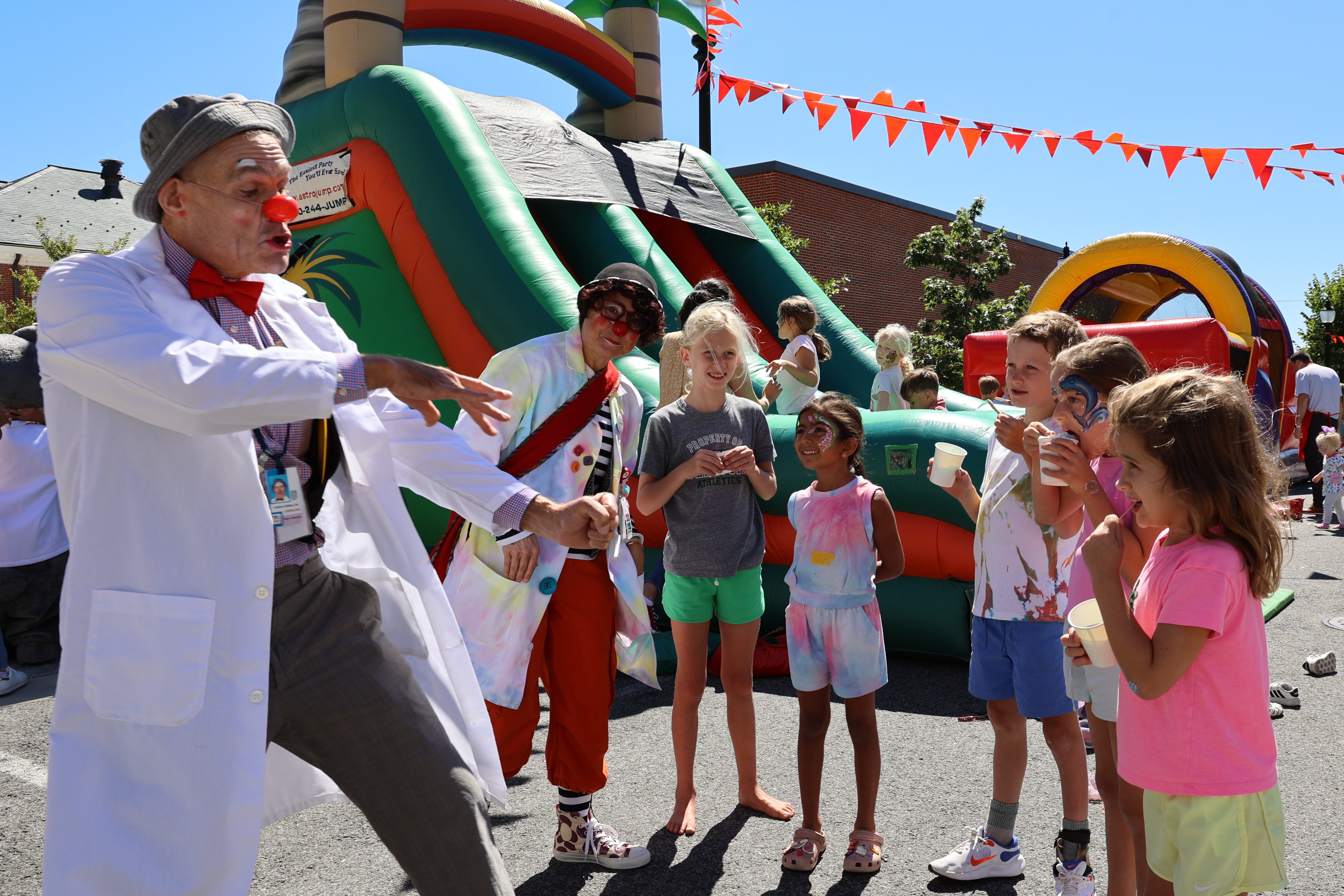Two clowns entertain a group of children in front of a large inflatable slide.