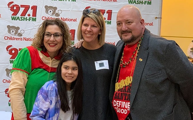 On air radio personalities pose with a parent and child at a radiothon event.
