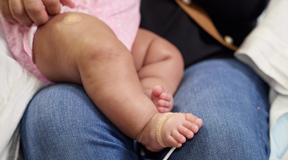 An infant's legs and feet while sitting on caregiver's lap.