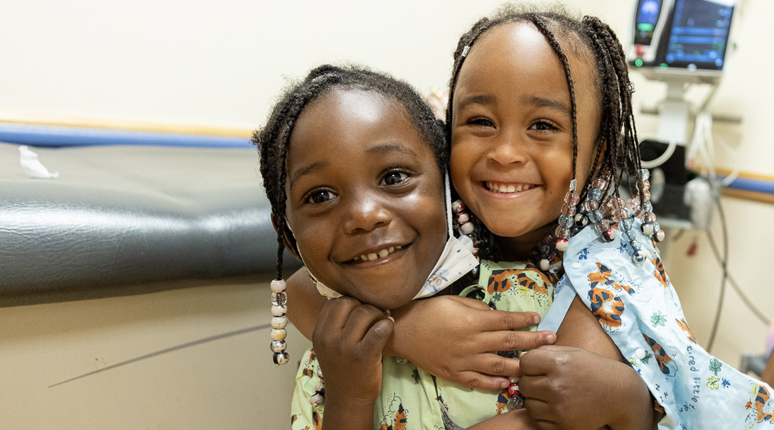 Two elementary school aged Black girls embrace warmly.