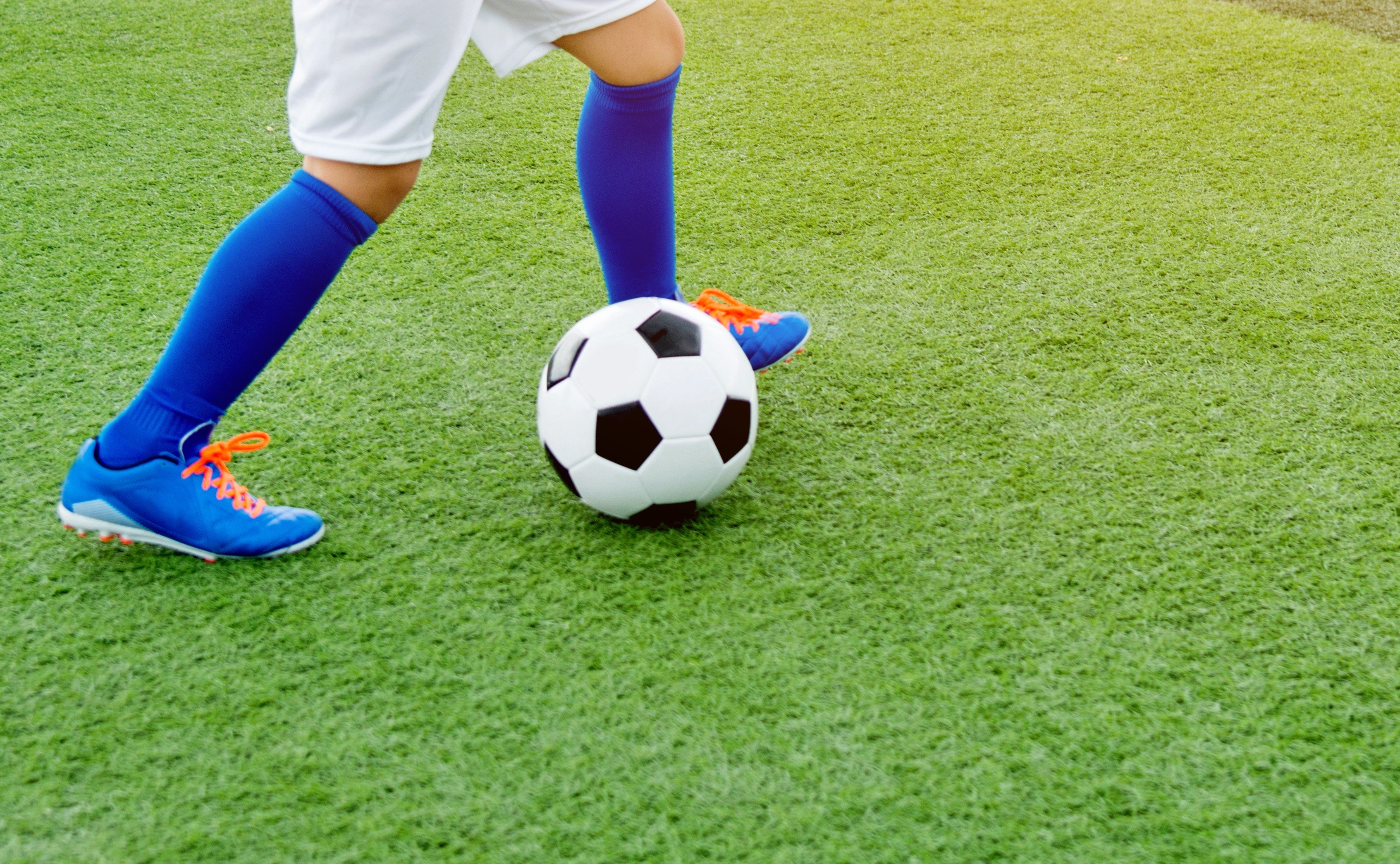 Zoomed in view of child's legs and feet kicking a soccer ball.