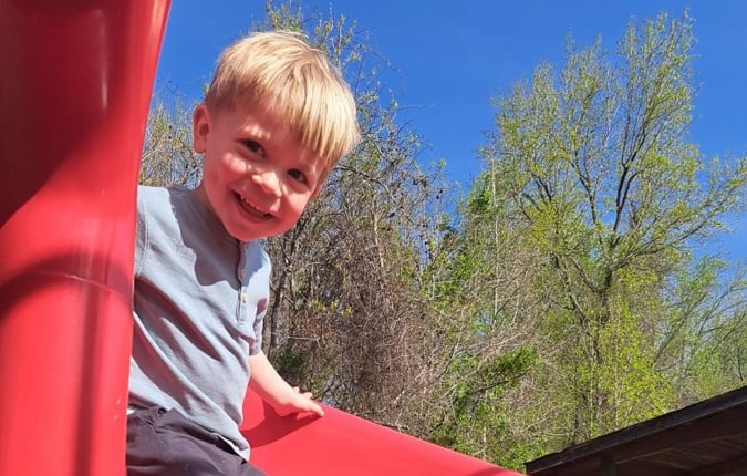 A White pre-school aged male patient plays on a playground slide.