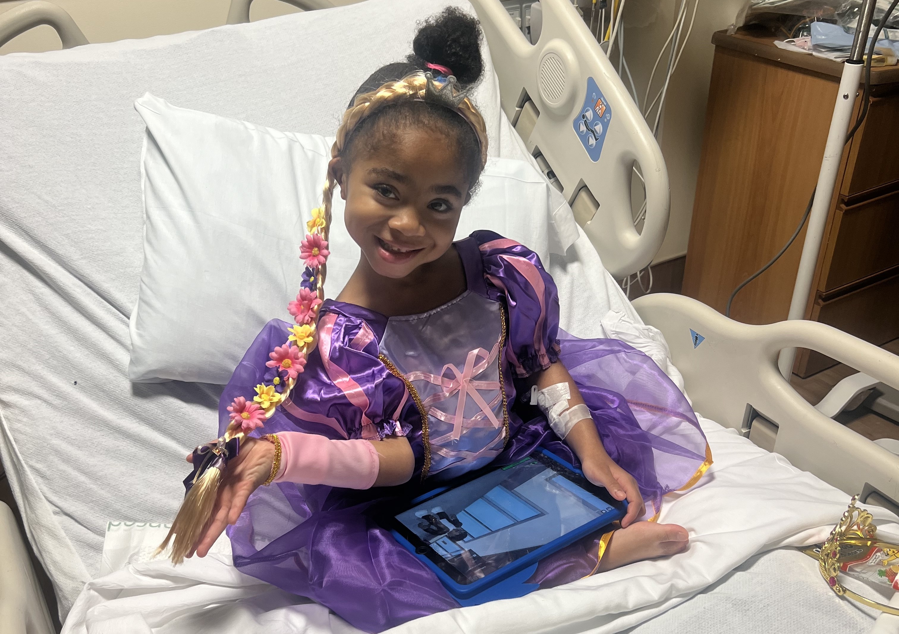 Zariyah smiling and wearing a Frozen princess dress while sitting in a hospital bed.