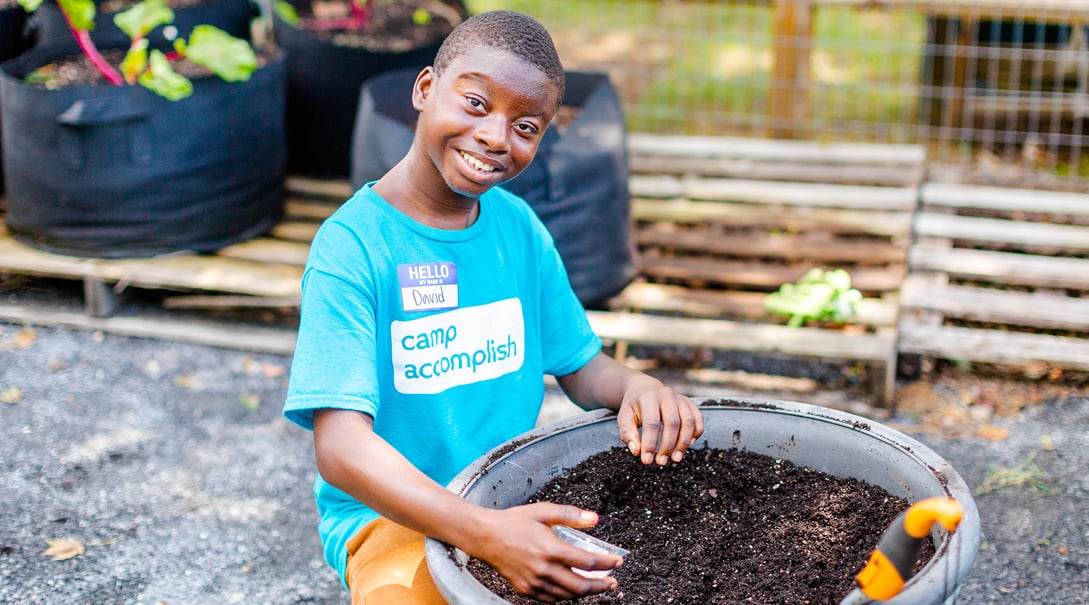 A young male camper smiles while working with gardening soil.