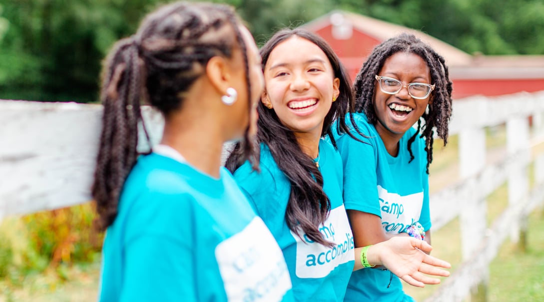 Three adolescent female campers of color smile and laugh together.
