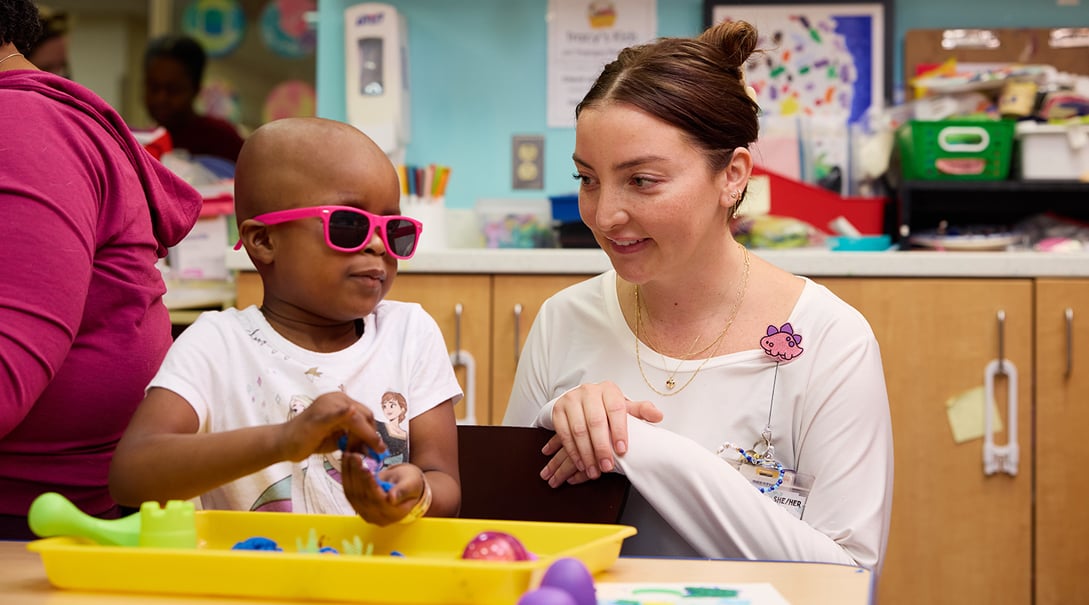 A young patient explores a tray of sensory objects while wearing sunglasses in the Tracy's Kids art therapy studio.