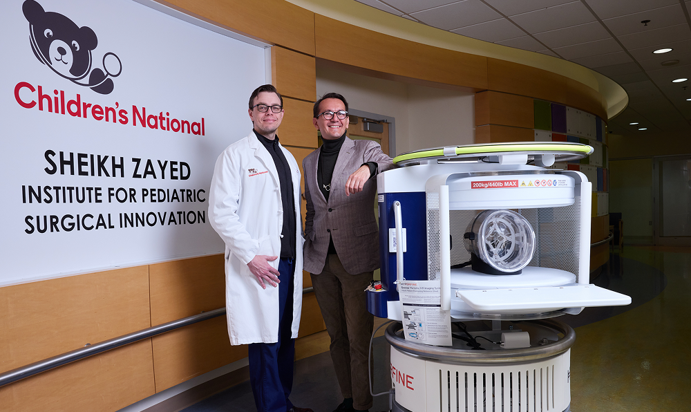 Drs. Linguraru and Donoho pose with the Hyperfine Swoop in front of the Sheikh Zayed Institute for Pediatric Surgical Innovation sign.